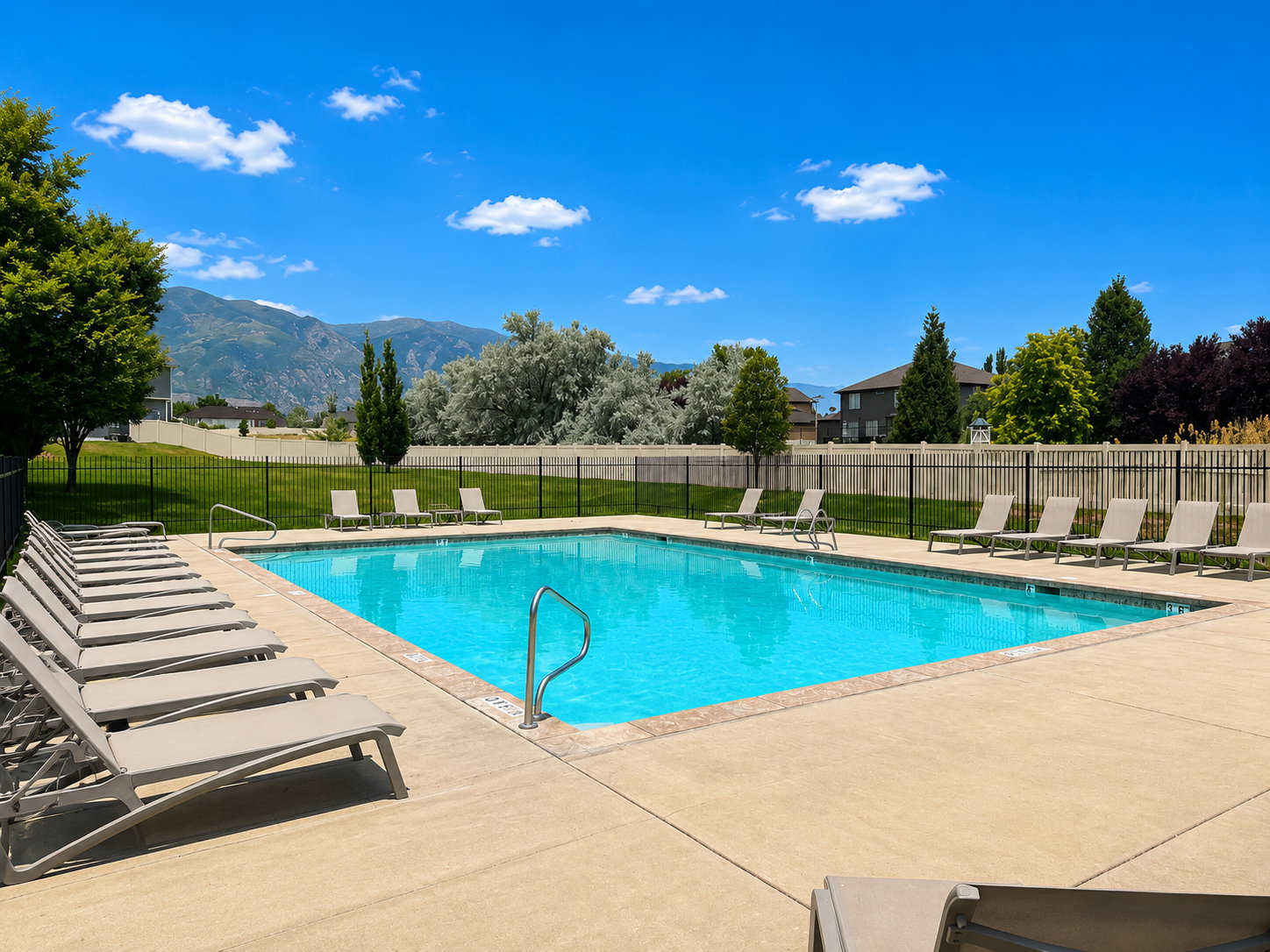 Rectangular swimming pool featuring a concrete deck surround, perimeter fencing, and mature trees