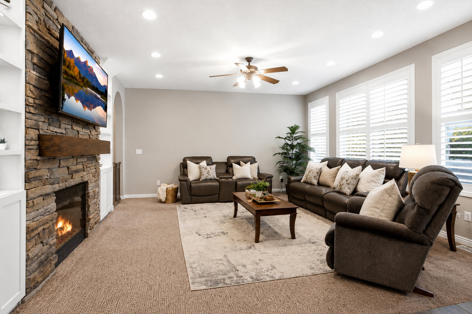Spacious living area featuring a stone-clad fireplace with a wood mantle, built-in shelving, recessed lighting, and multiple windows with plantation shutters