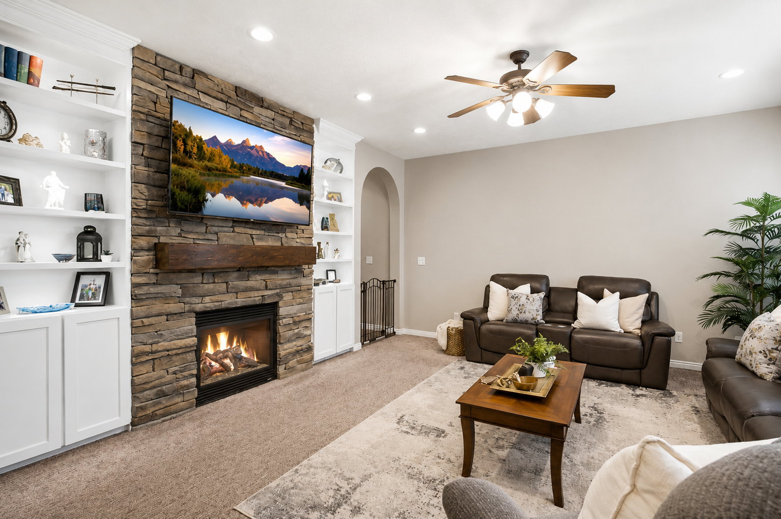 Living area featuring a stone-clad fireplace with a wood-finish mantel, flanked by built-in shelving and cabinetry