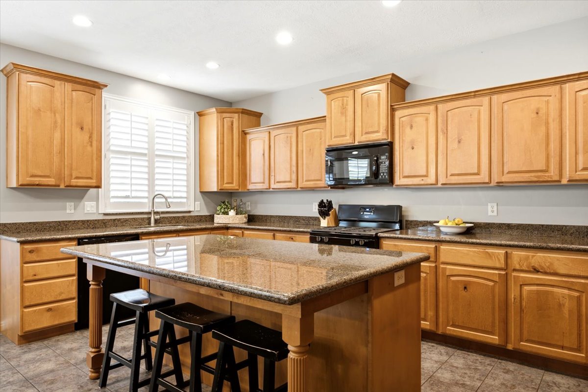 Spacious kitchen featuring light wood cabinetry, granite countertops, a central island with bar seating, and tile flooring