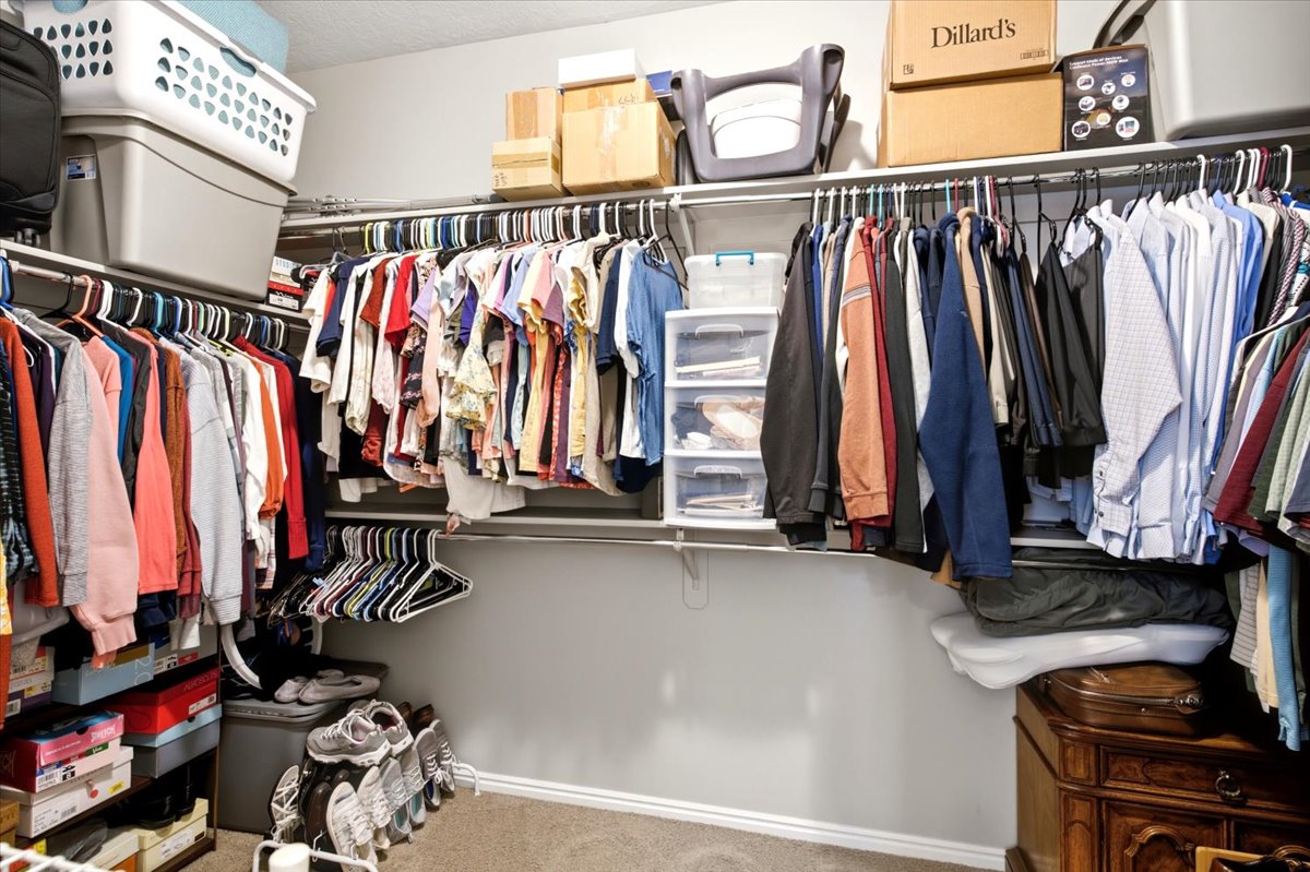 Walk-in closet featuring carpet flooring, white baseboards, and built-in shelving with multiple hanging rods