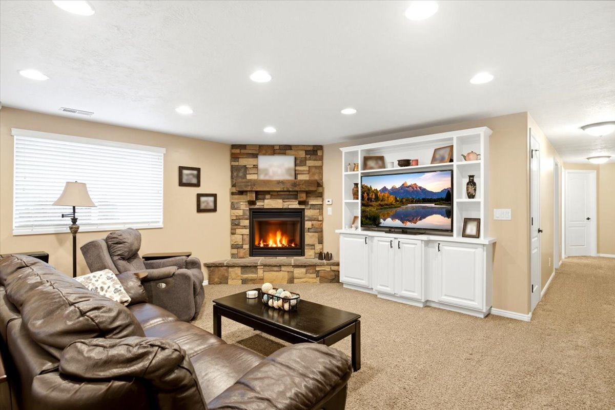 Living area featuring a stone-clad fireplace with a wood mantle, a built-in white media console with shelving, recessed lighting, and neutral-toned carpeting