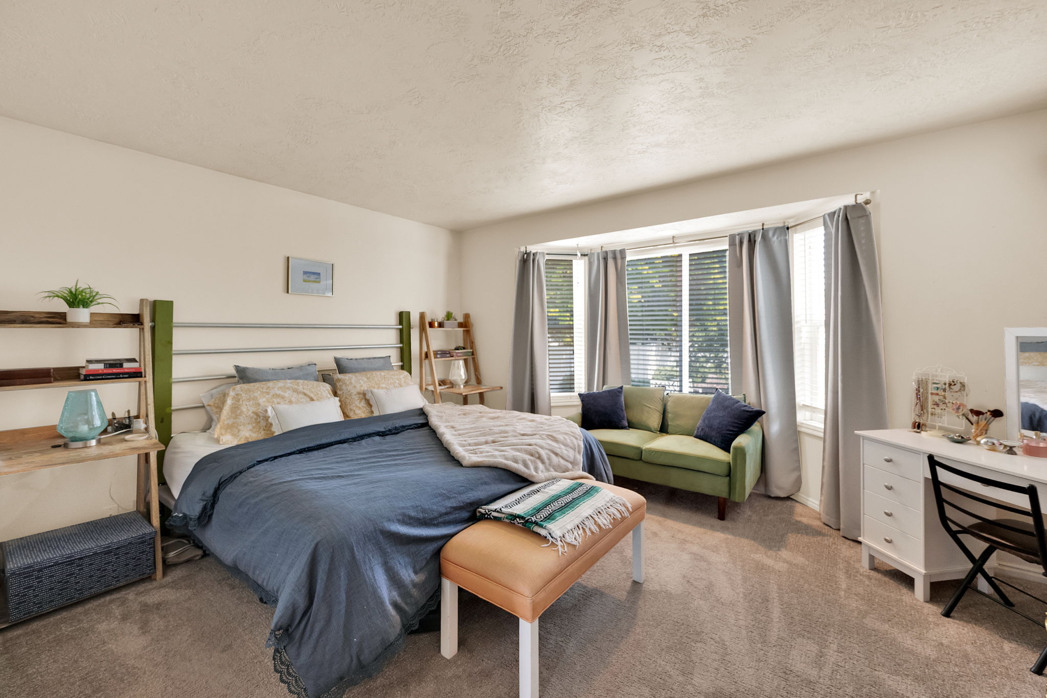 Carpeted bedroom featuring a bay window, window treatments, and neutral wall tones