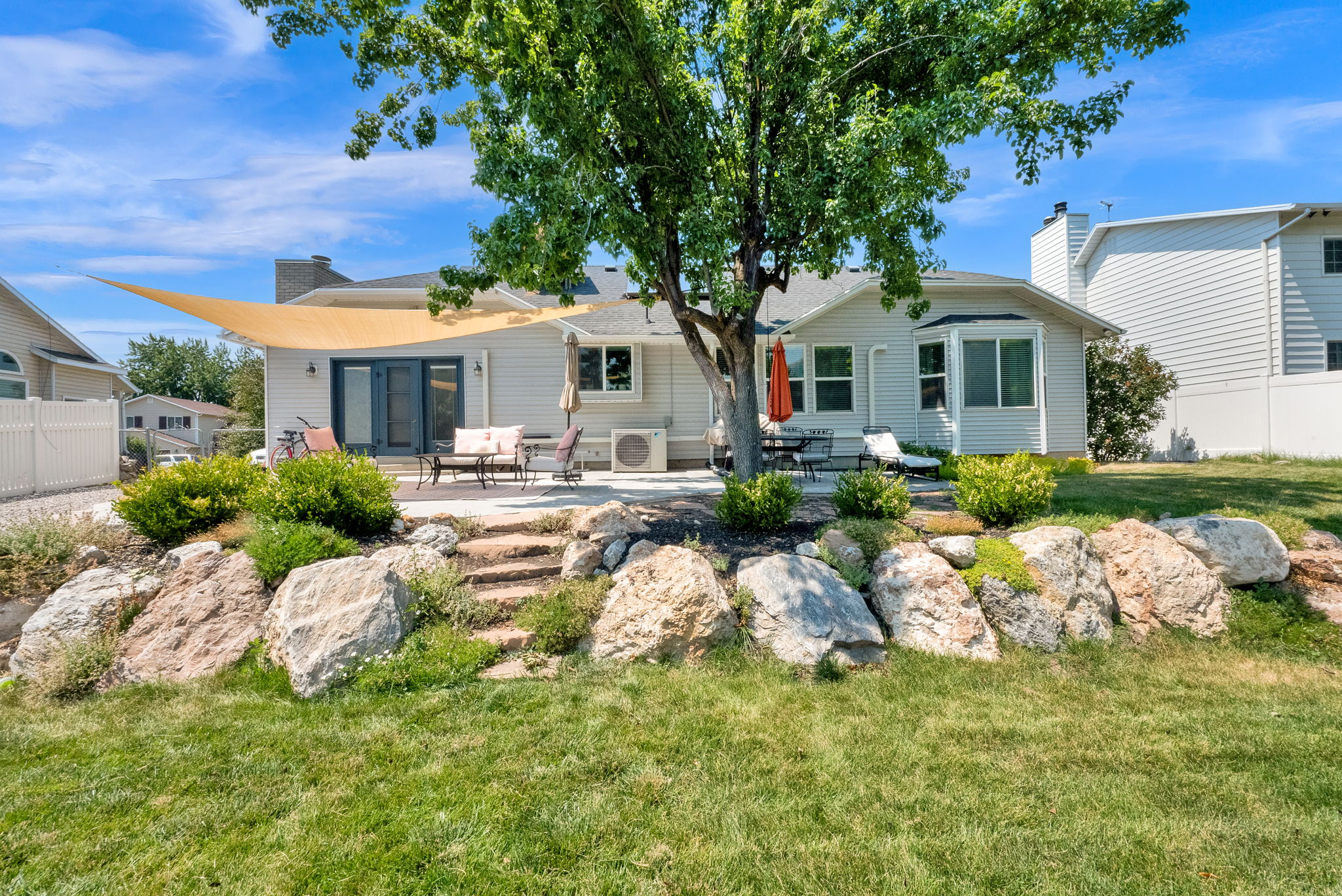 Rear exterior featuring a stone retaining wall, terraced landscaping, and a concrete patio with dual French doors
