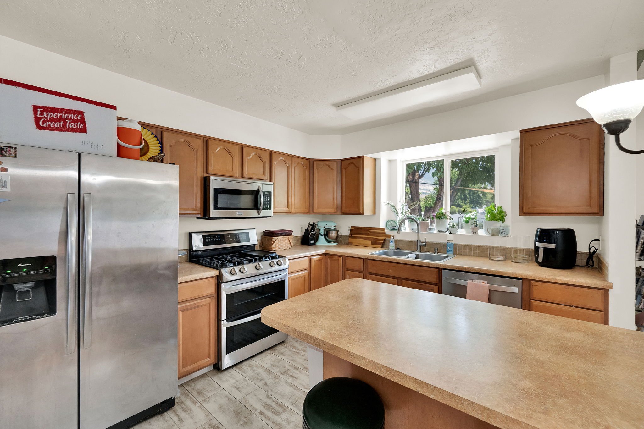 Kitchen featuring wood-finish cabinetry, stainless steel appliances, a double basin sink, and an island with countertop seating