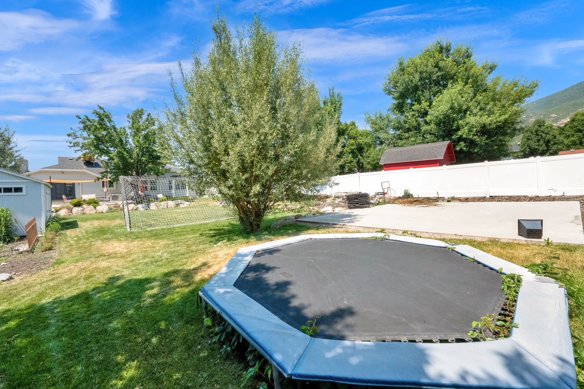 Expansive backyard featuring a large concrete patio, a white vinyl privacy fence, and a red shed with a dark roof