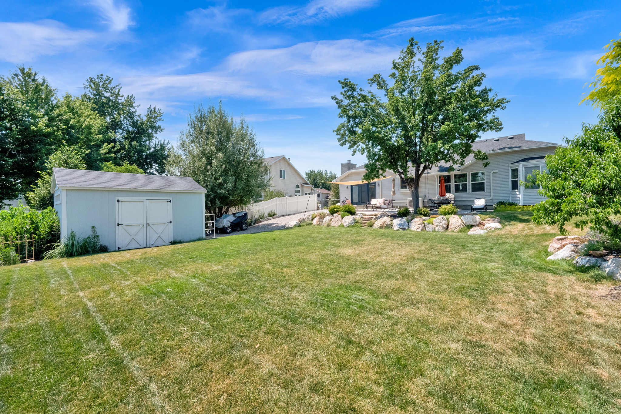 Expansive rear yard featuring a large lawn, detached storage shed with double doors, and a stone-lined terraced patio area