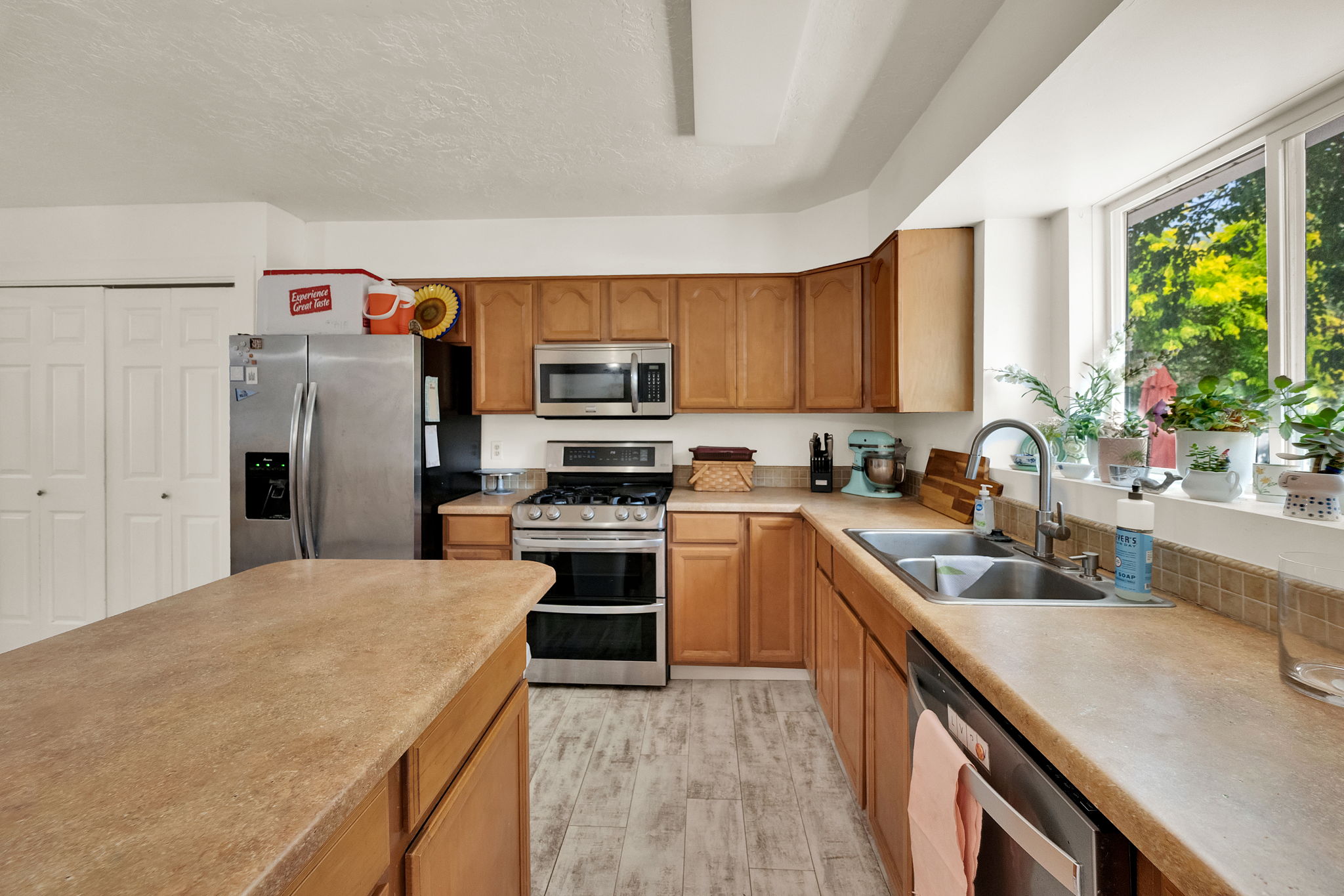 Kitchen featuring wood-finish flooring, light wood cabinetry, stainless steel appliances, and a large window above the sink