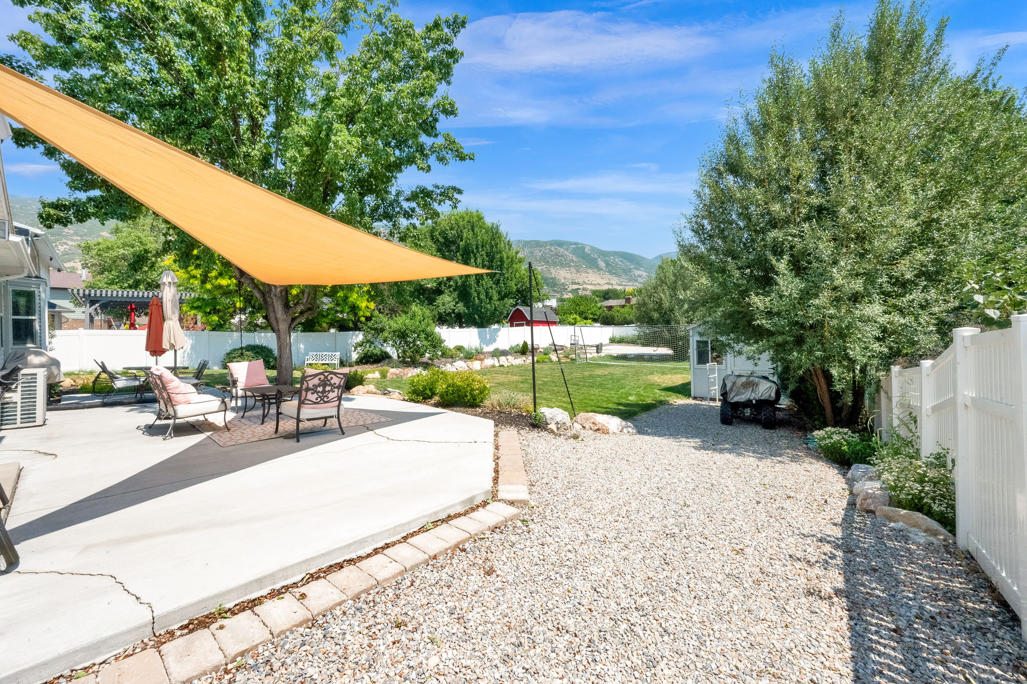 Expansive concrete patio with a shade sail, bordered by a white privacy fence