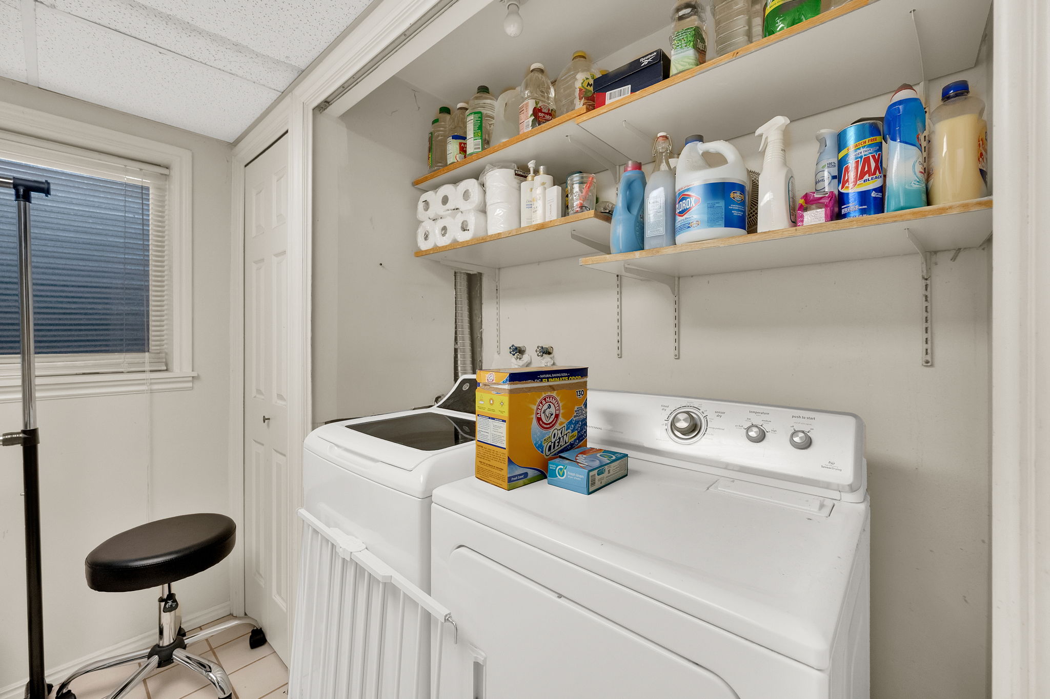 Dedicated laundry area featuring a window with horizontal blinds, built-in shelving, white paneled walls, and a tiled floor