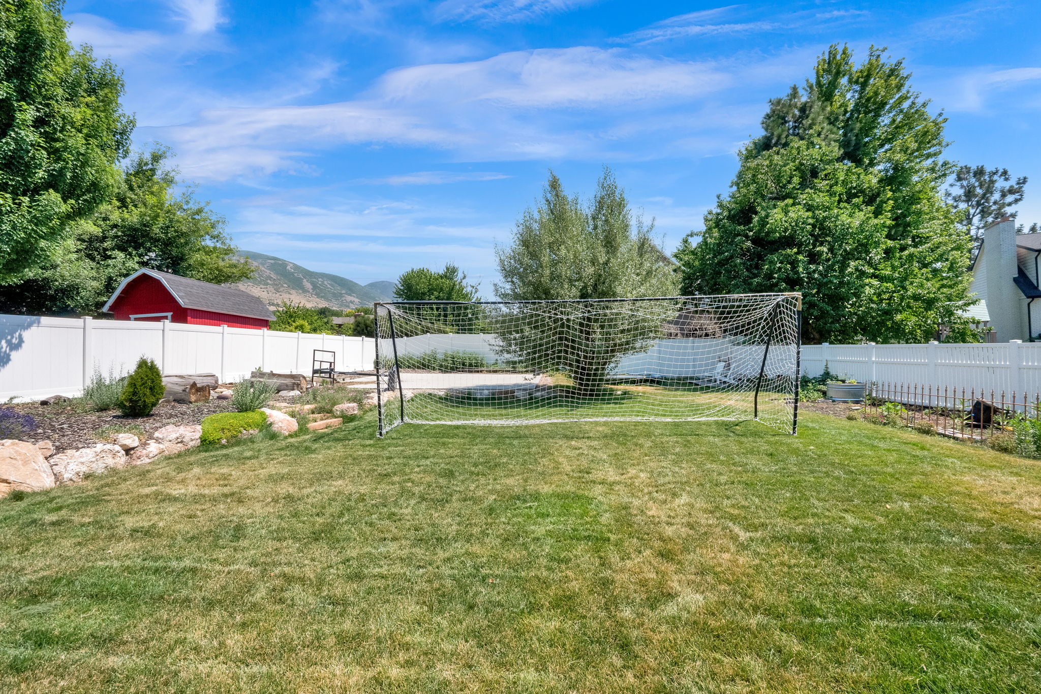 Expansive backyard featuring a lush lawn, white privacy fencing, and a red shed