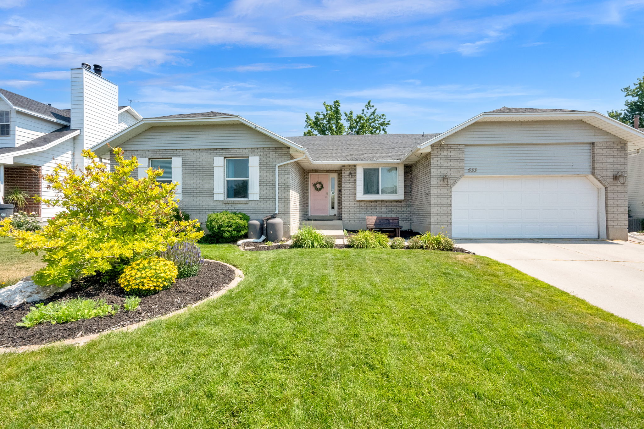 Front exterior showcasing a light brick facade, a two-car garage, and a manicured lawn