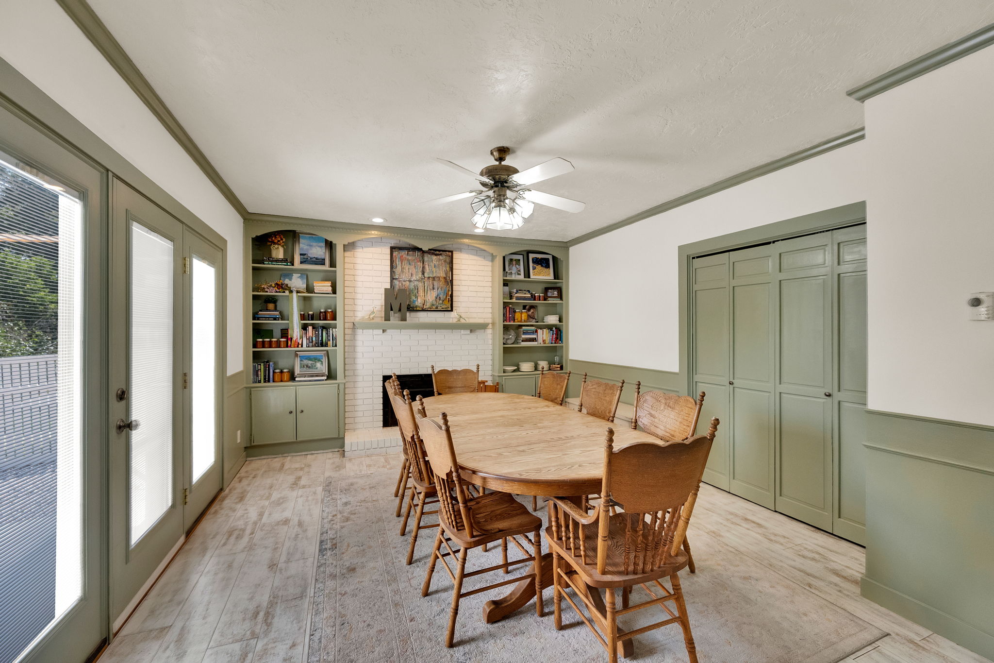 Dining area featuring wood-finish flooring, a white brick fireplace with mantel, built-in shelving, a ceiling fan, and French doors