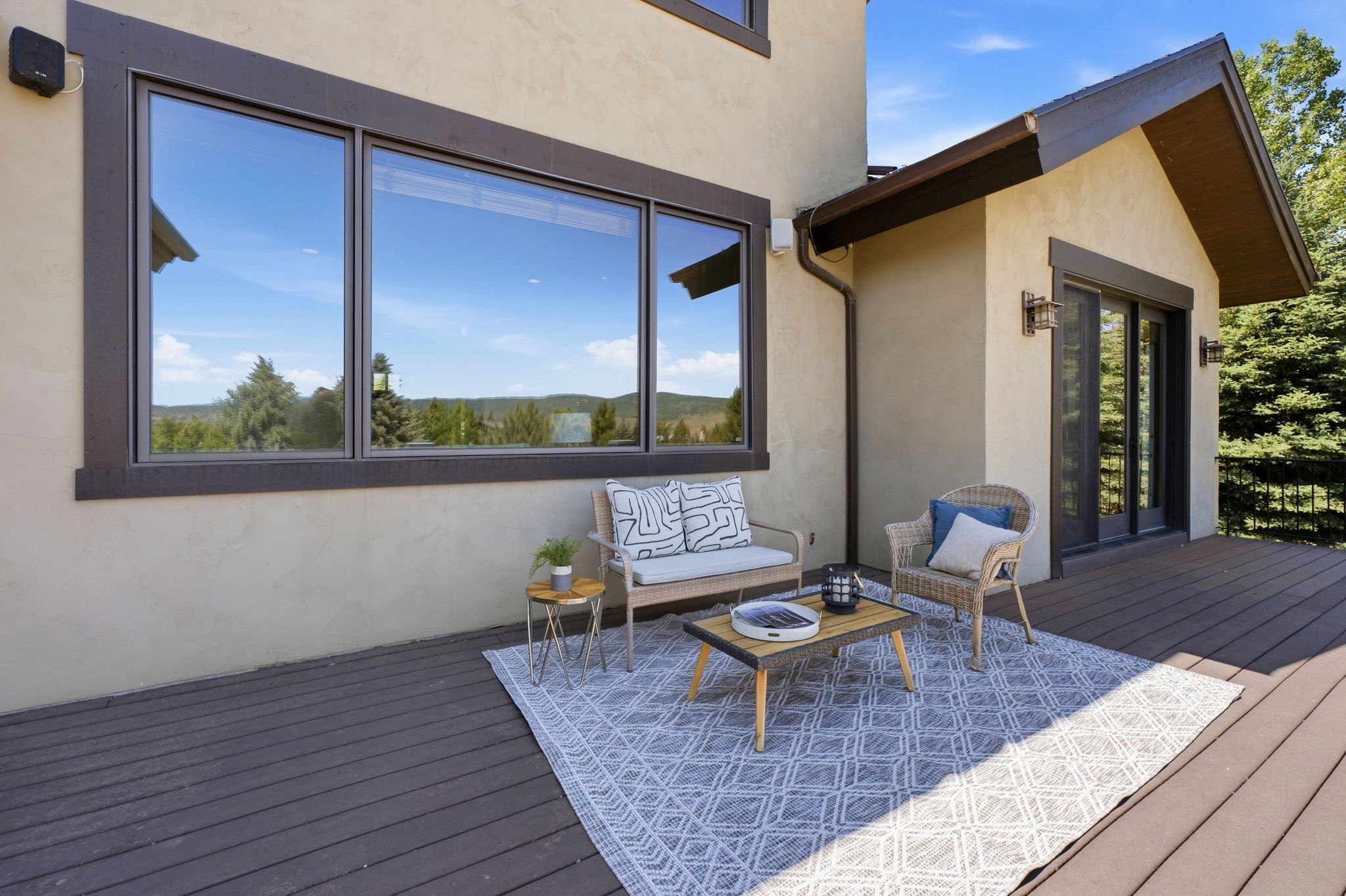 Expansive outdoor deck featuring composite decking, a stucco exterior, large picture windows, and a sliding glass door with dual outdoor sconces