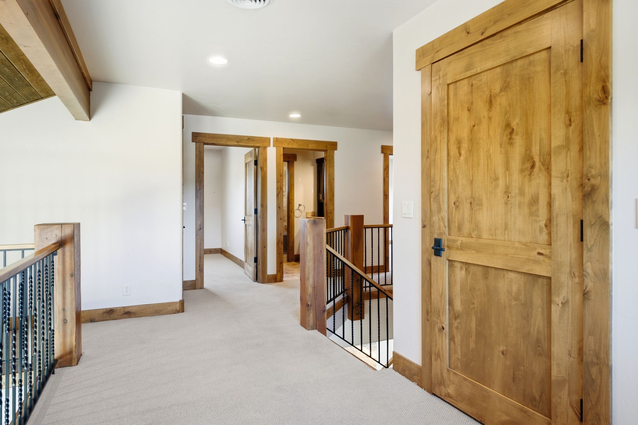 Hallway featuring light wood doors and trim, neutral carpet flooring, recessed lighting, and a wood and iron baluster railing