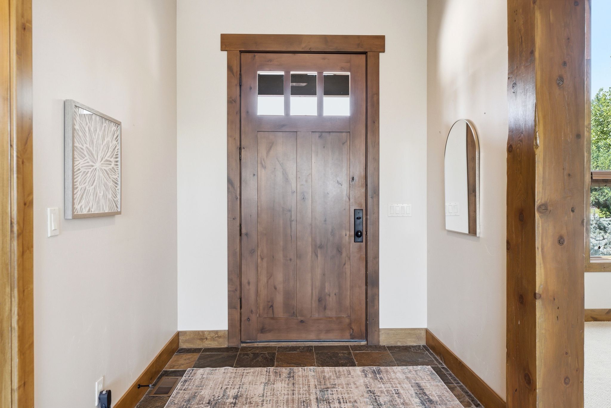 Solid wood entry door with upper glass panels and matte black hardware, framed by wide wood trim
