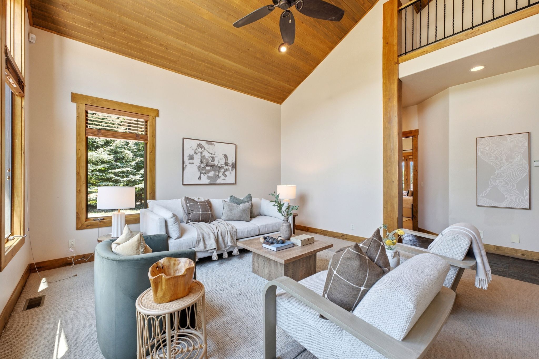Vaulted wood-paneled ceilings with ceiling fan, large picture windows with wood trim, and an exposed wood beam detail