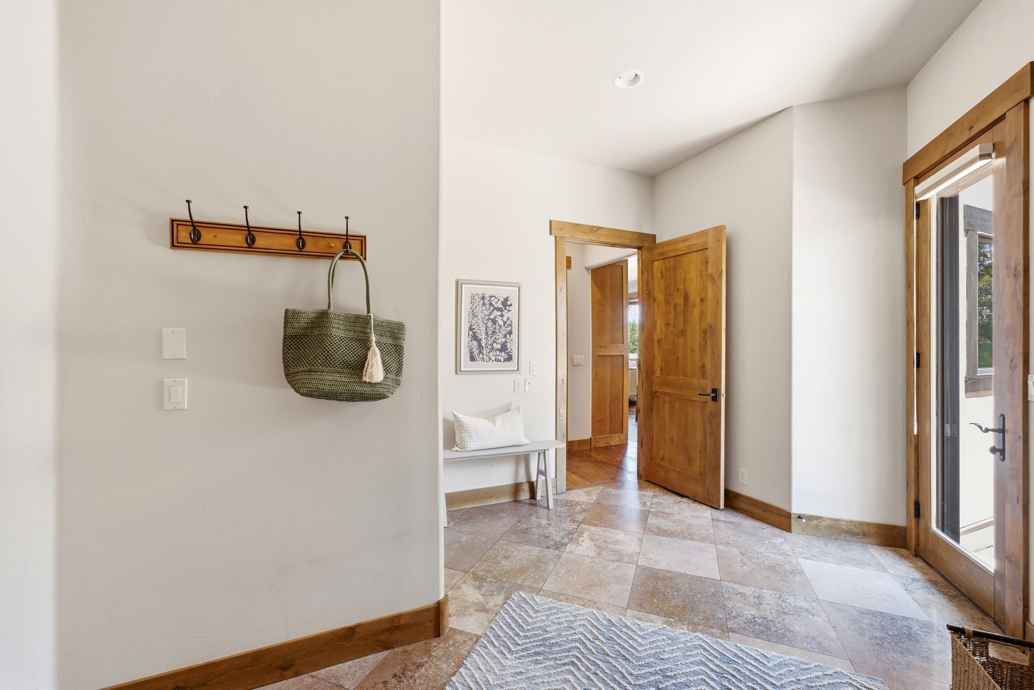 Entryway featuring natural wood trim, a built-in coat rack, and light-colored tile flooring