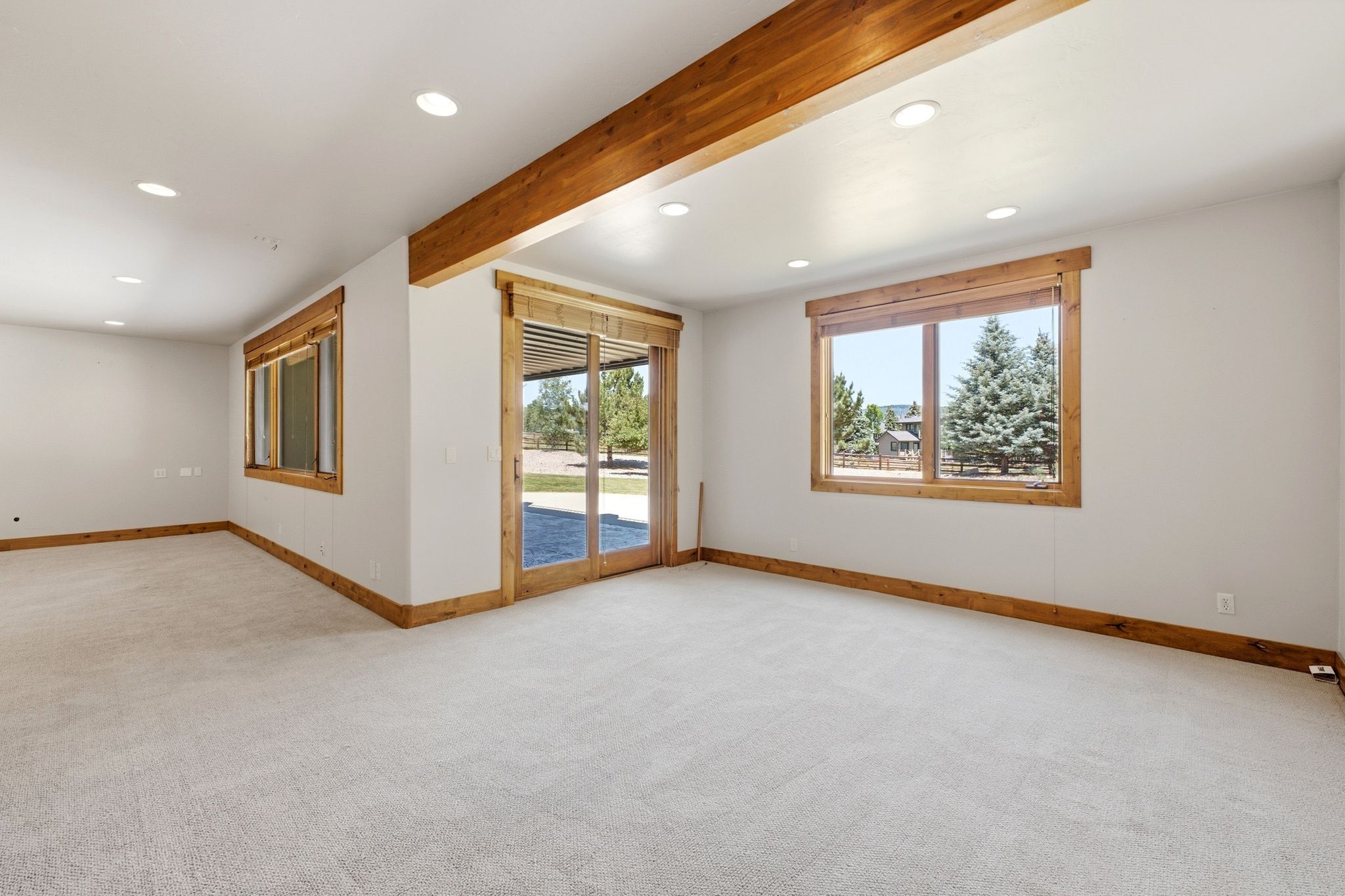Carpeted room featuring exposed wood beams, recessed lighting, wood-trimmed windows, and a glass sliding door to the exterior