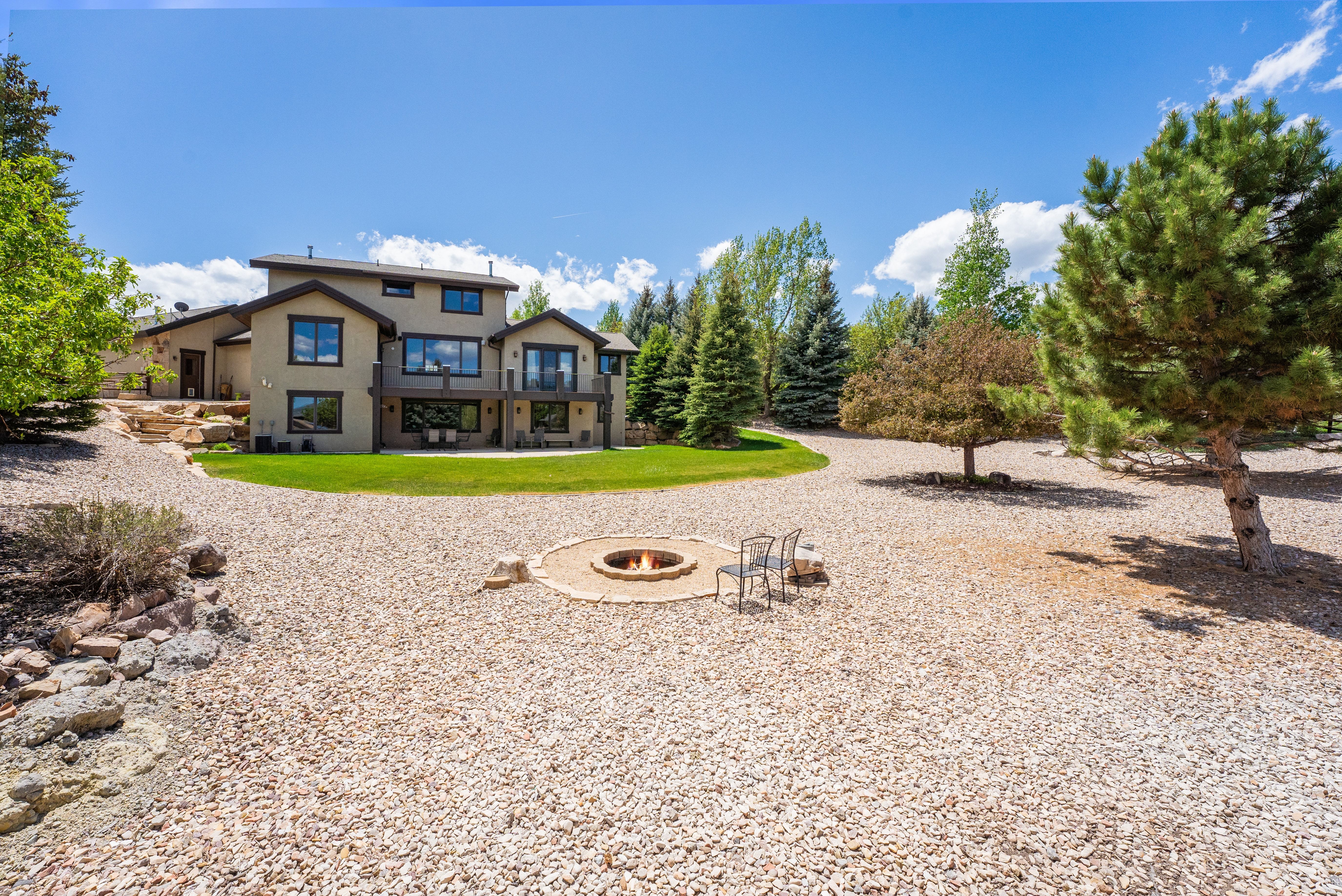 Expansive backyard featuring a central rock fire pit, gravel landscaping, and mature trees