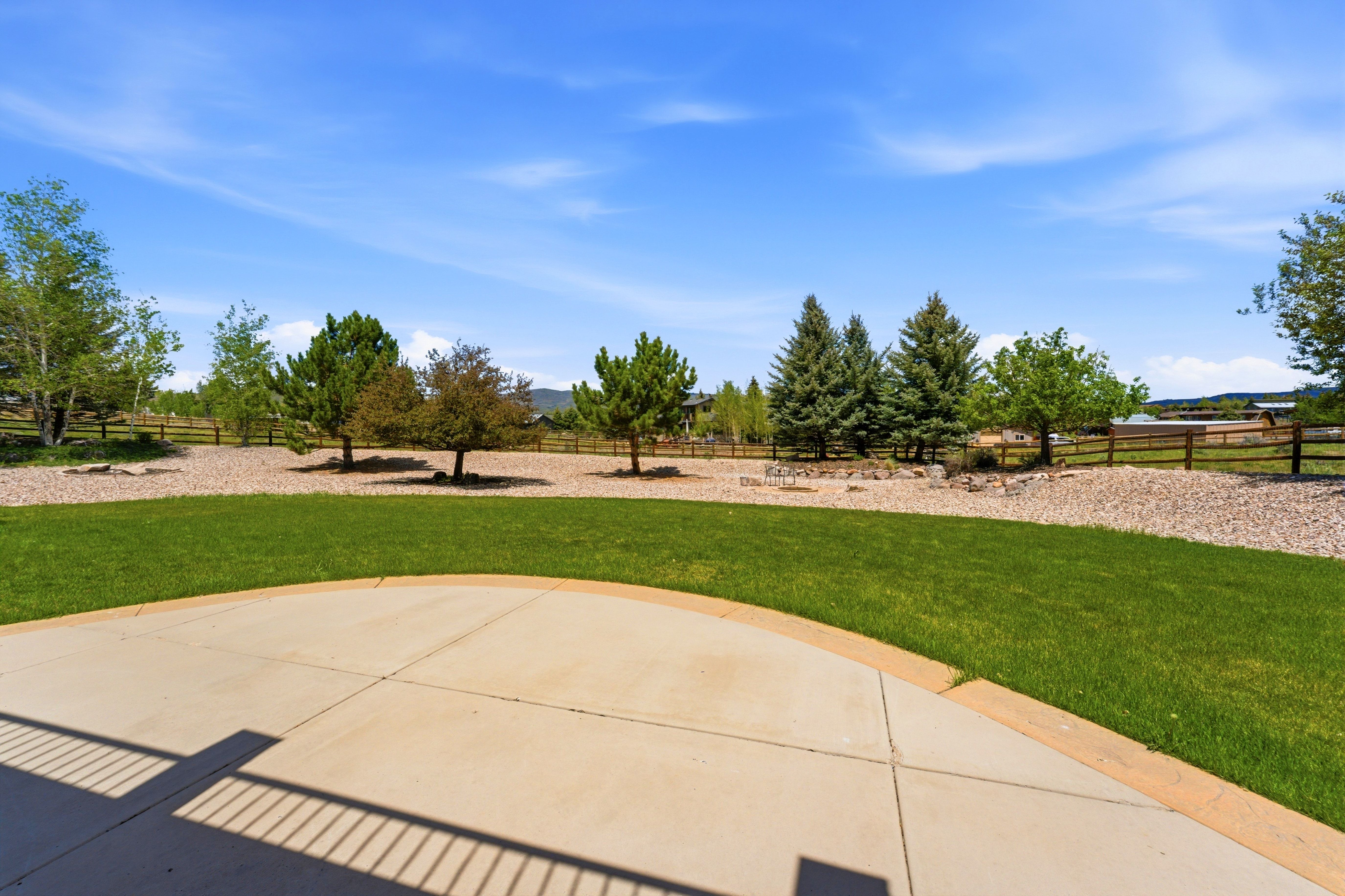 Concrete patio opening to a spacious lawn with a gravel border and mature trees