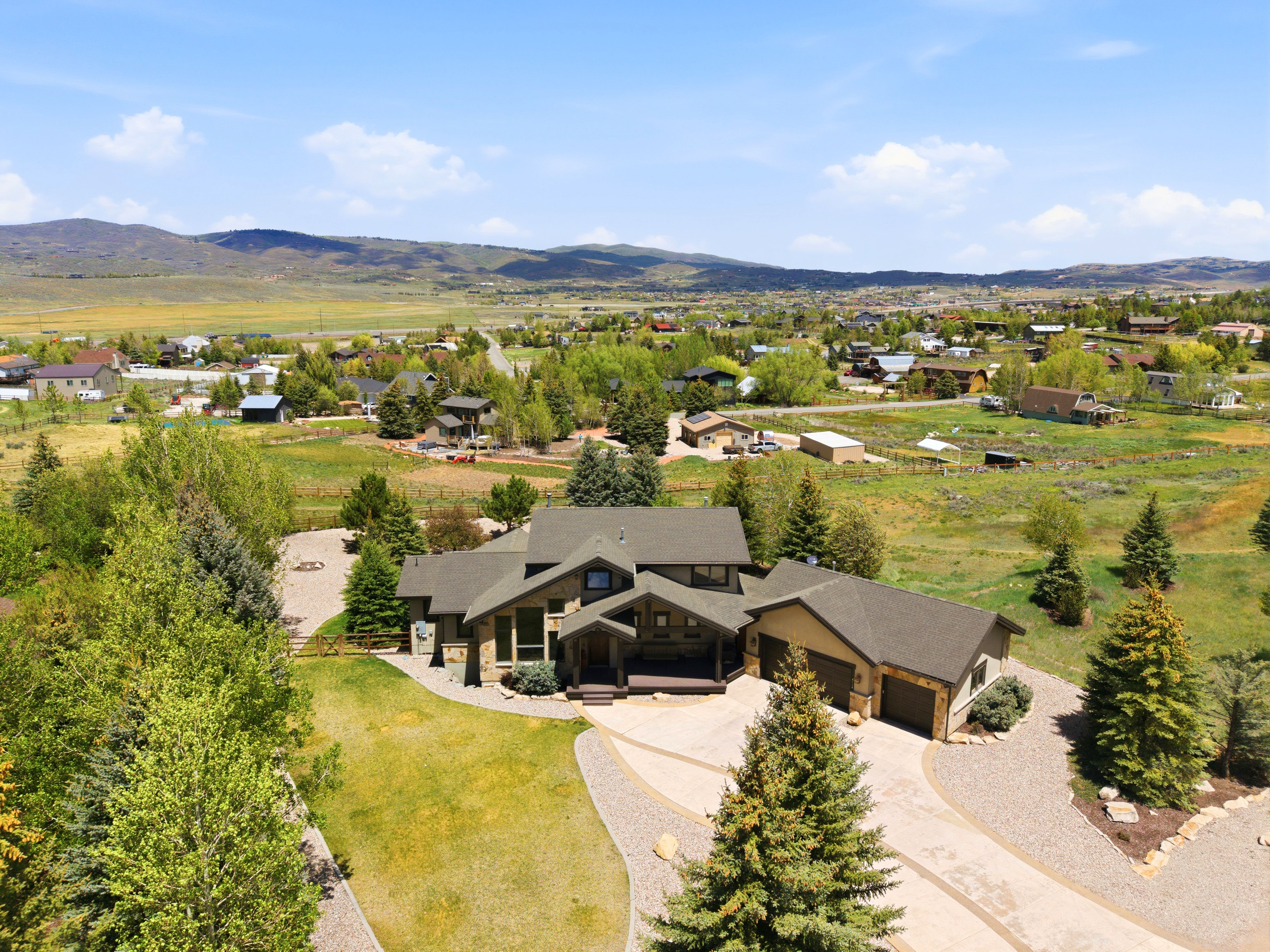 Stone and wood-sided residence featuring a multi-car garage, expansive driveway, mature landscaping, and a surrounding natural landscape