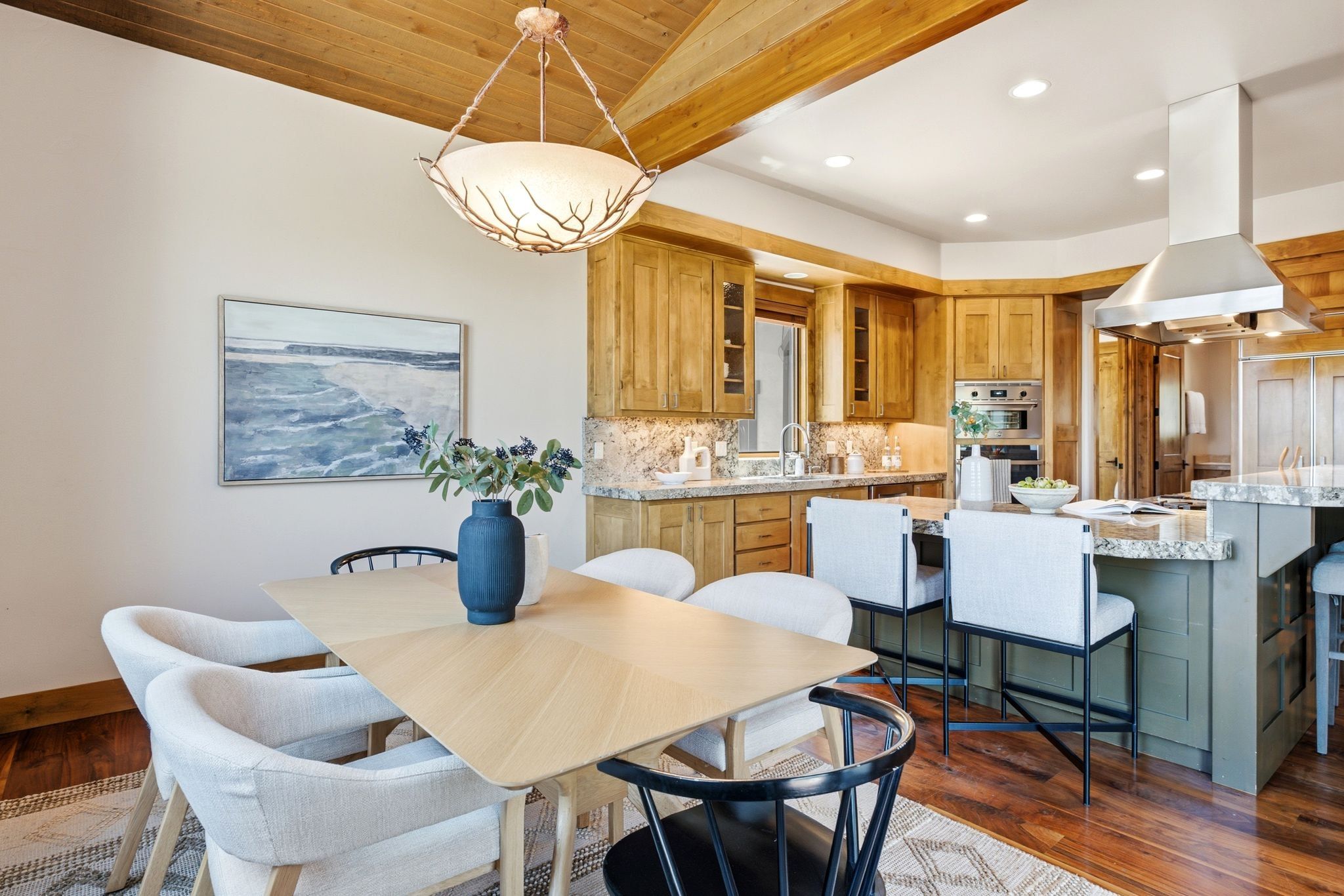 Open-concept kitchen and dining area featuring wood-finish flooring, a wood-paneled ceiling with exposed beams, and a decorative pendant light fixture