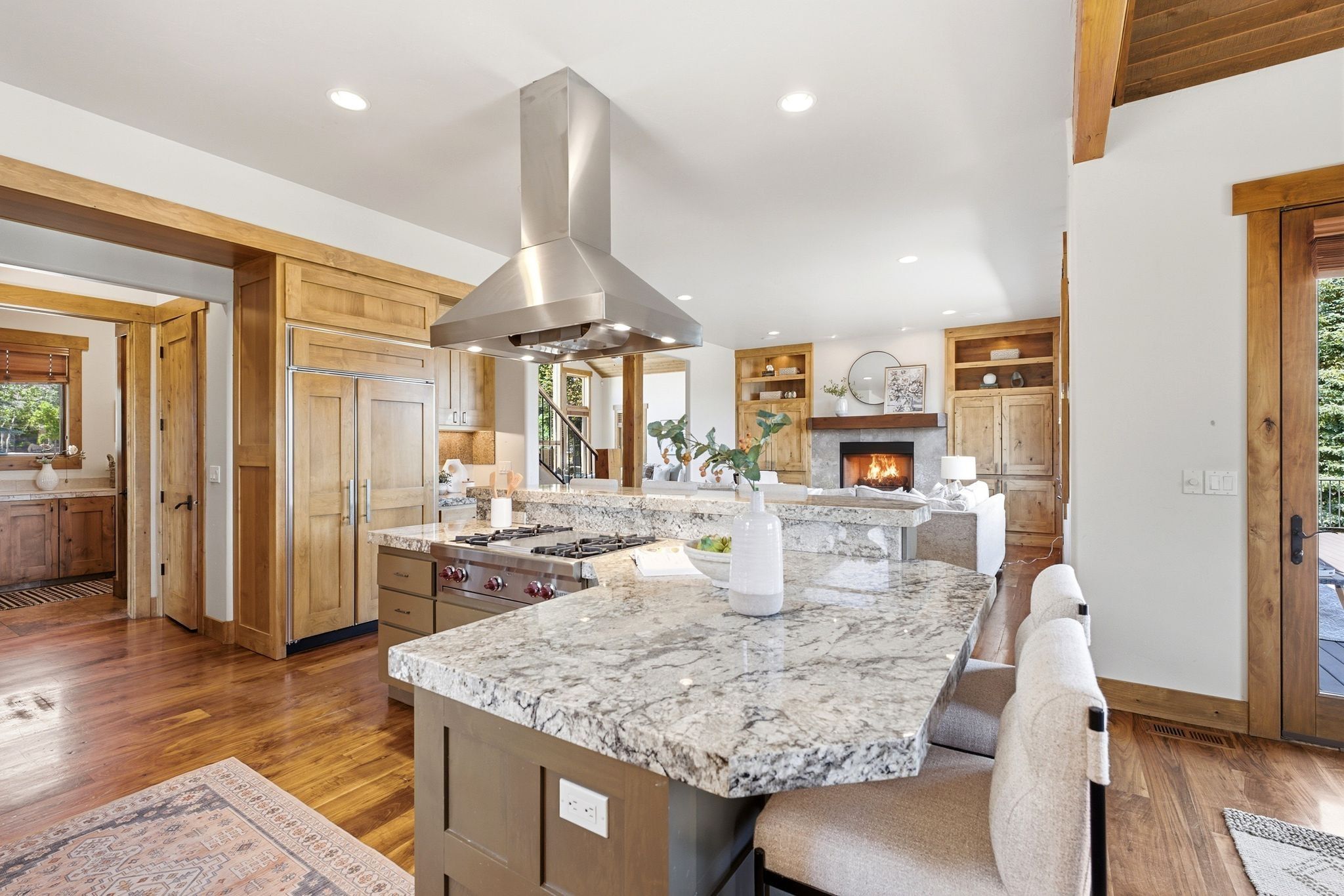 Gourmet kitchen featuring a large island with granite countertops, a built-in cooktop with a stainless steel vent hood, integrated paneled refrigerator, and wood-finish flooring