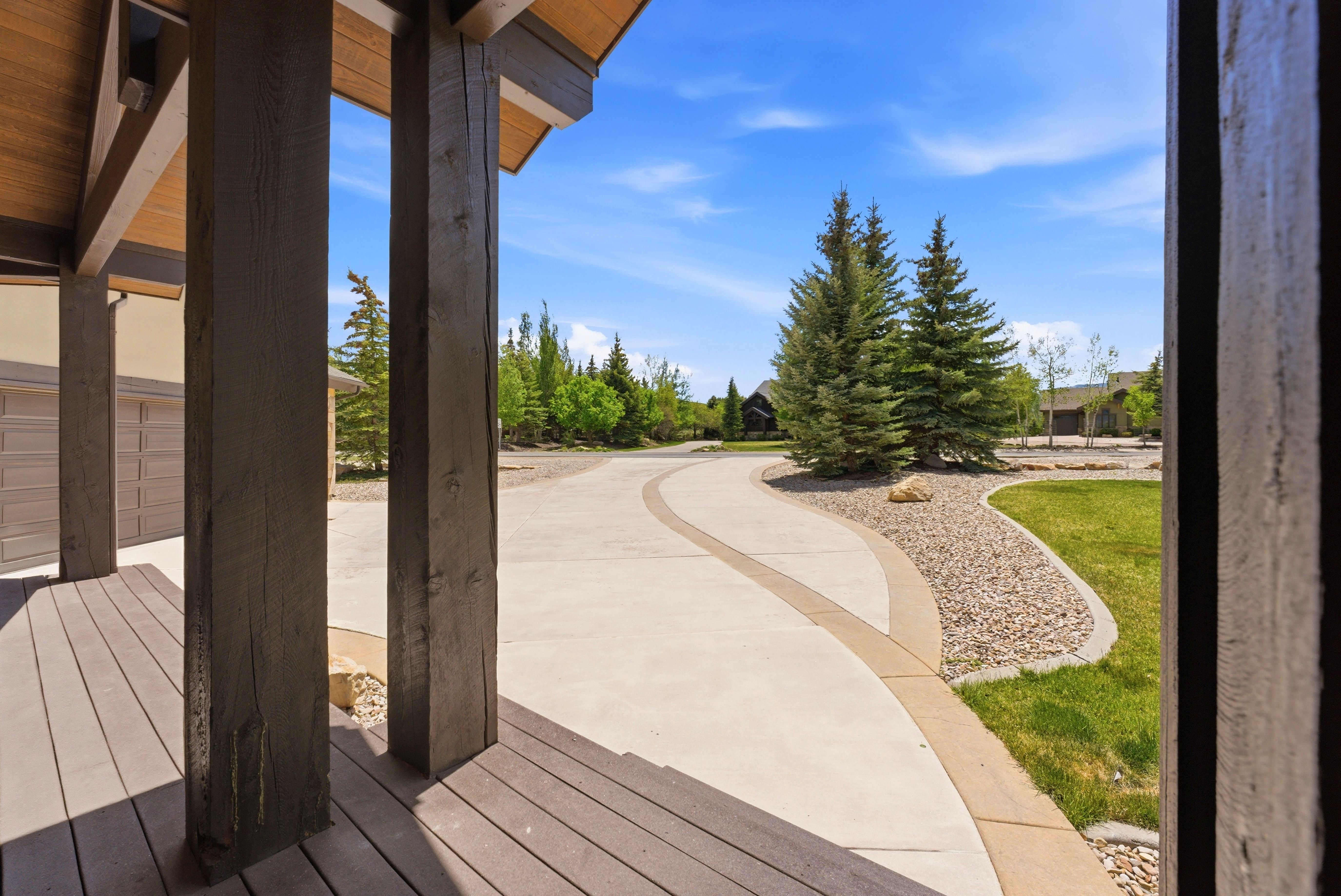 Expansive concrete driveway with decorative stone inlay, bordered by manicured gravel landscaping and mature evergreen trees