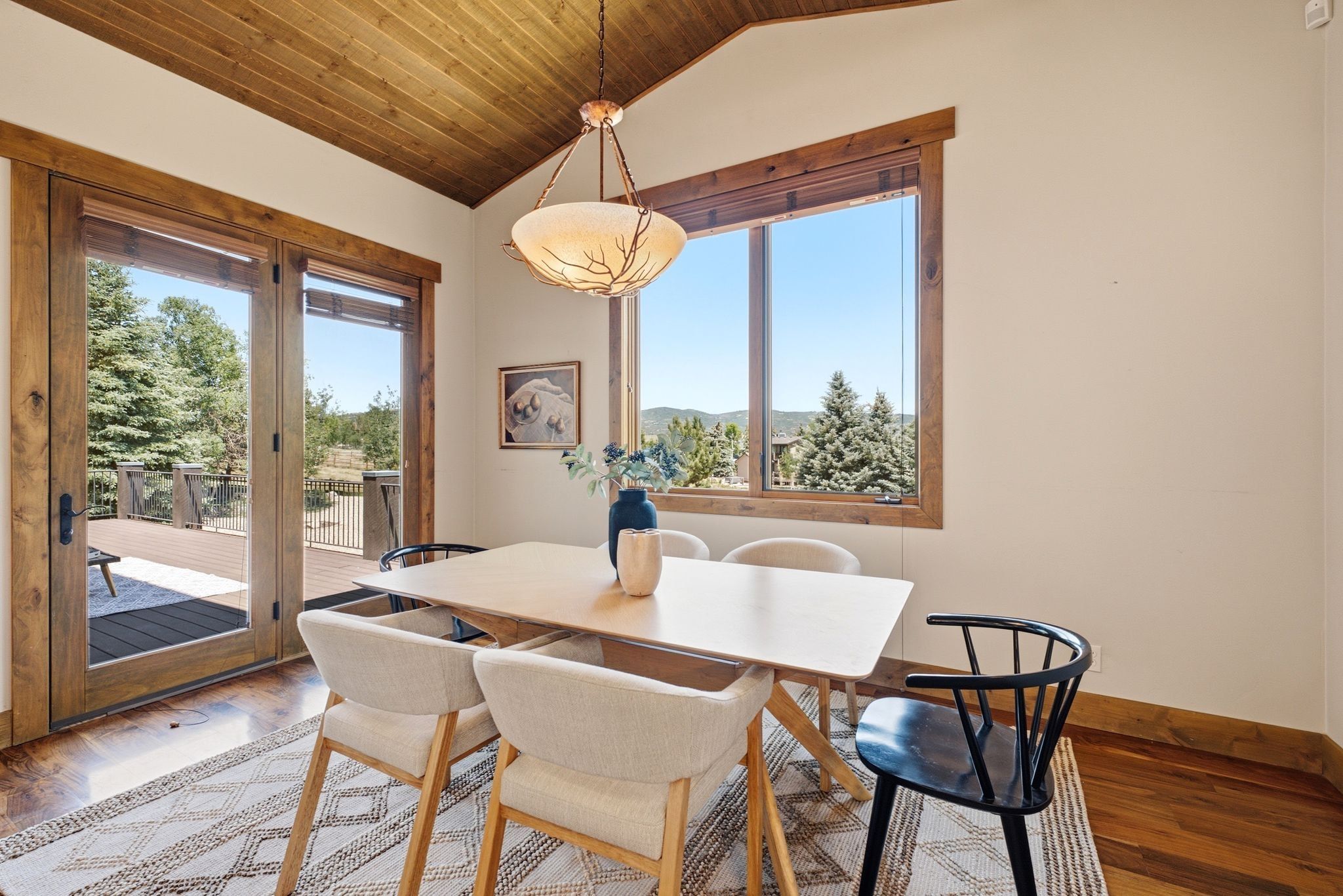 Vaulted wood-paneled ceiling with a decorative light fixture, hardwood flooring, and dual French doors opening to an exterior deck