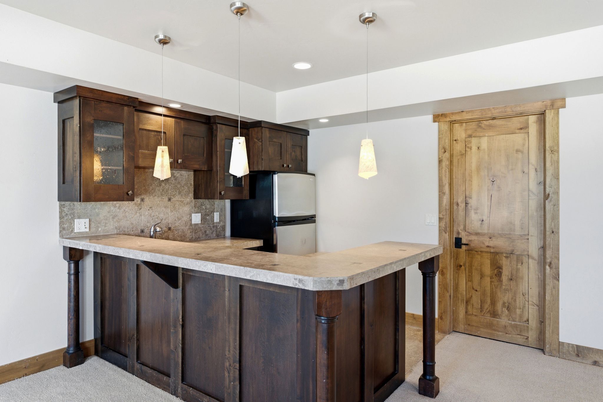 Wet bar featuring dark wood cabinetry, an integrated sink, and a stone-finish countertop