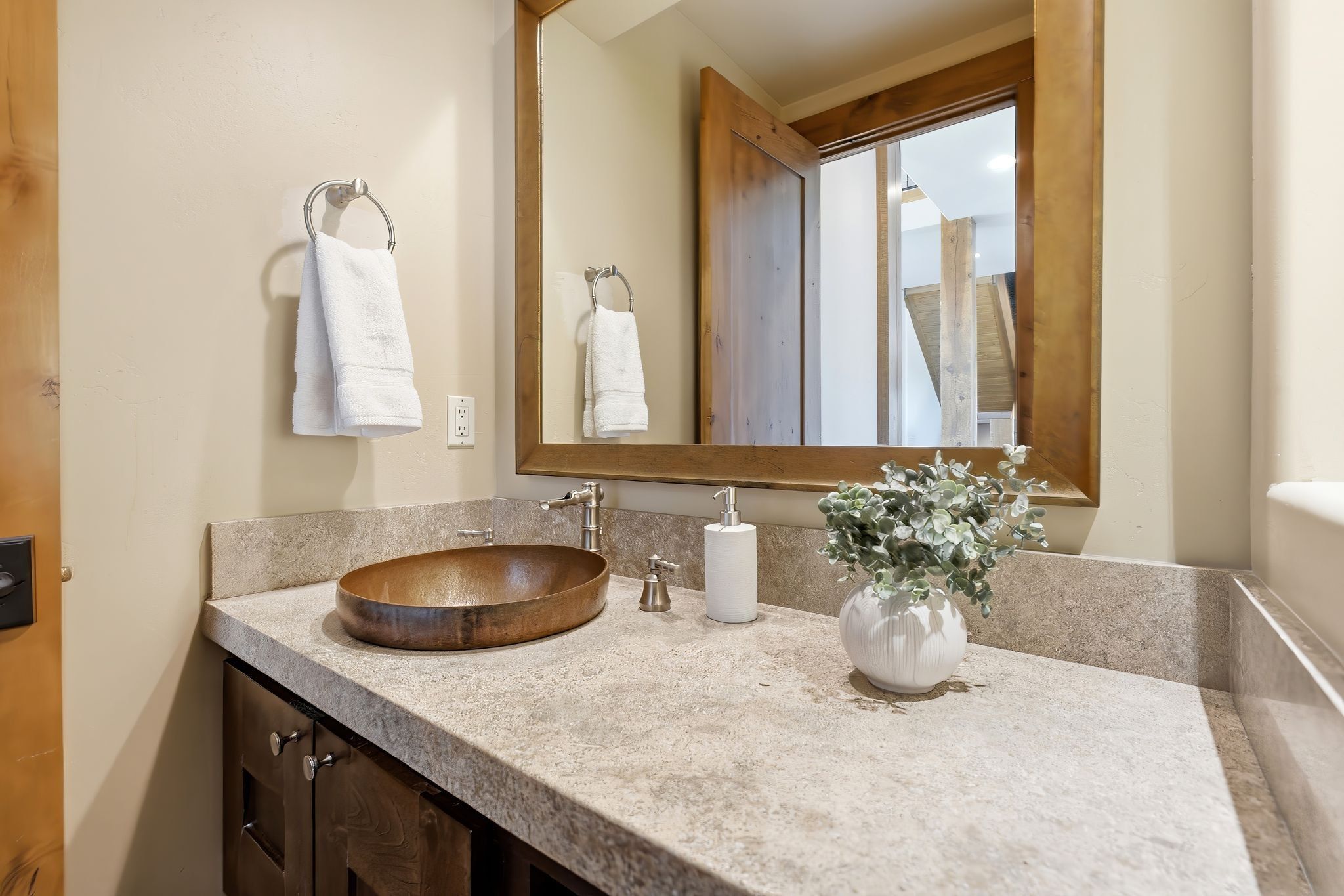 Bathroom vanity featuring a vessel sink, stone-finish countertop, and wood-framed mirror