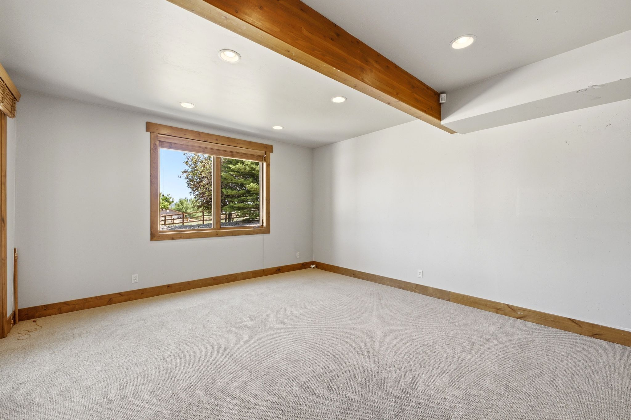 Bright interior space featuring a window with wood trim, wood beam ceiling accents, recessed lighting, and light-toned carpet flooring