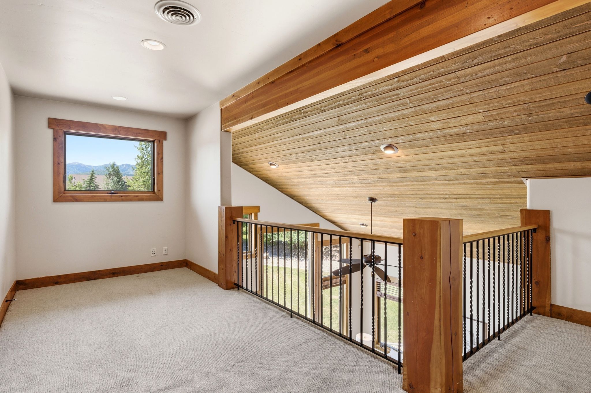 Carpeted loft featuring a wood-trimmed window with mountain scenery, a wood-paneled ceiling with recessed lighting, and a wrought iron railing with wood posts