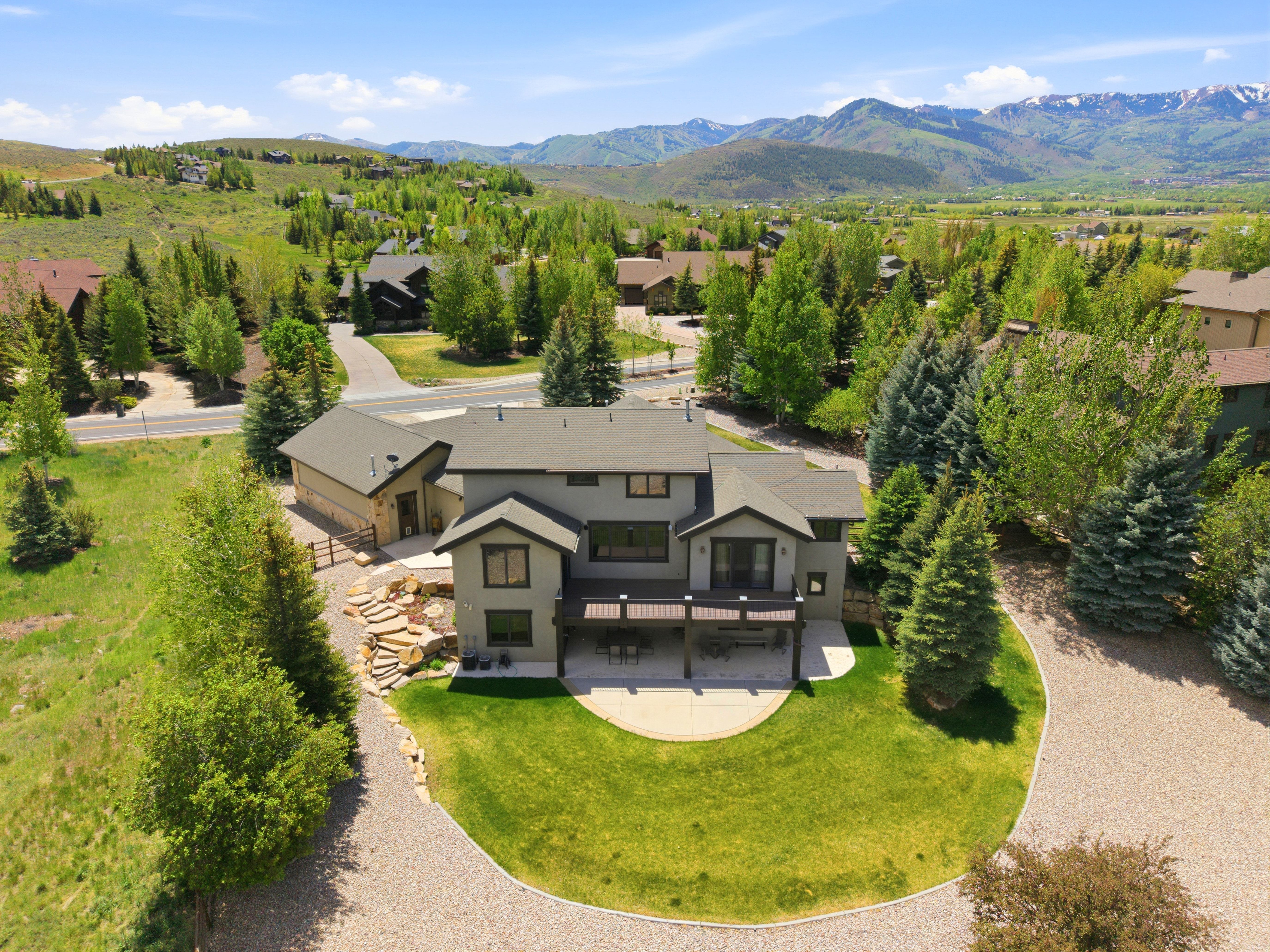 Contemporary residence featuring a gravel driveway, stone retaining walls, a terraced backyard, a spacious outdoor deck, and surrounding greenery
