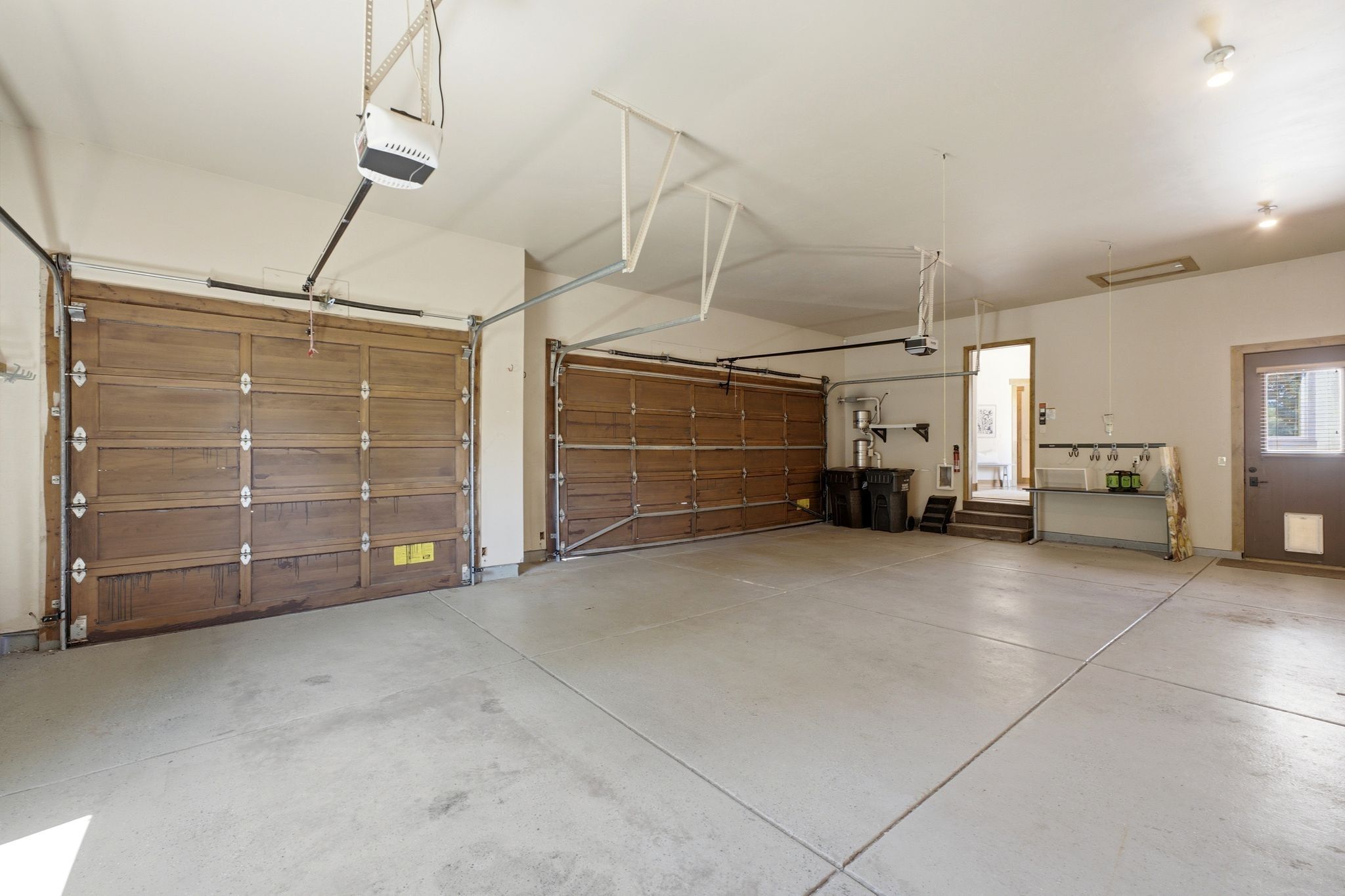 Spacious garage featuring two wood-panel garage doors, a concrete floor, and an integrated utility sink