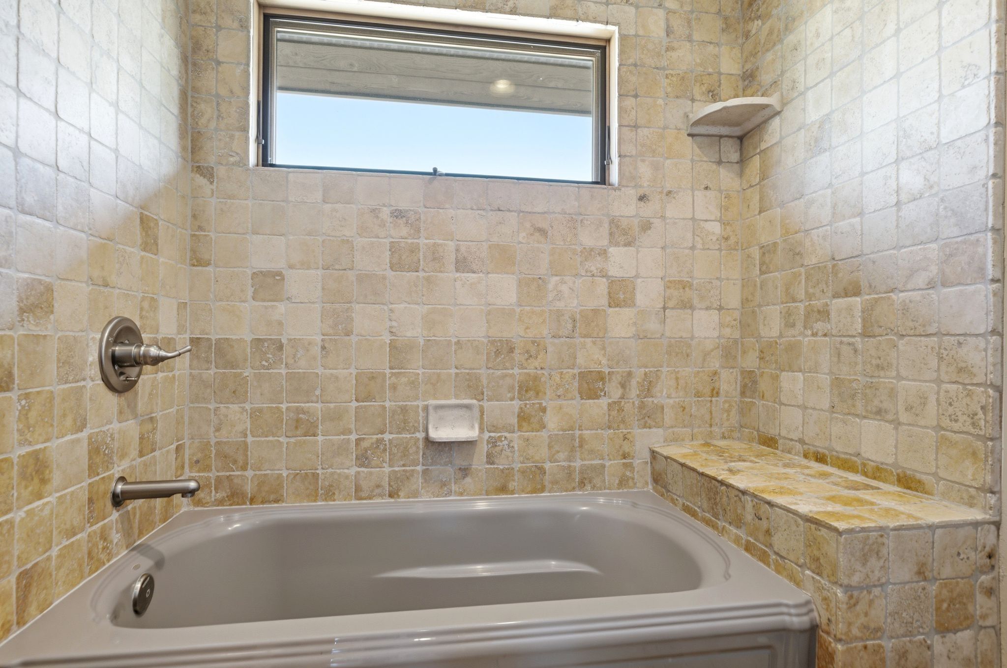 Bathtub enclosure featuring square tile surfacing, an integrated tile bench, and a corner tile shelf