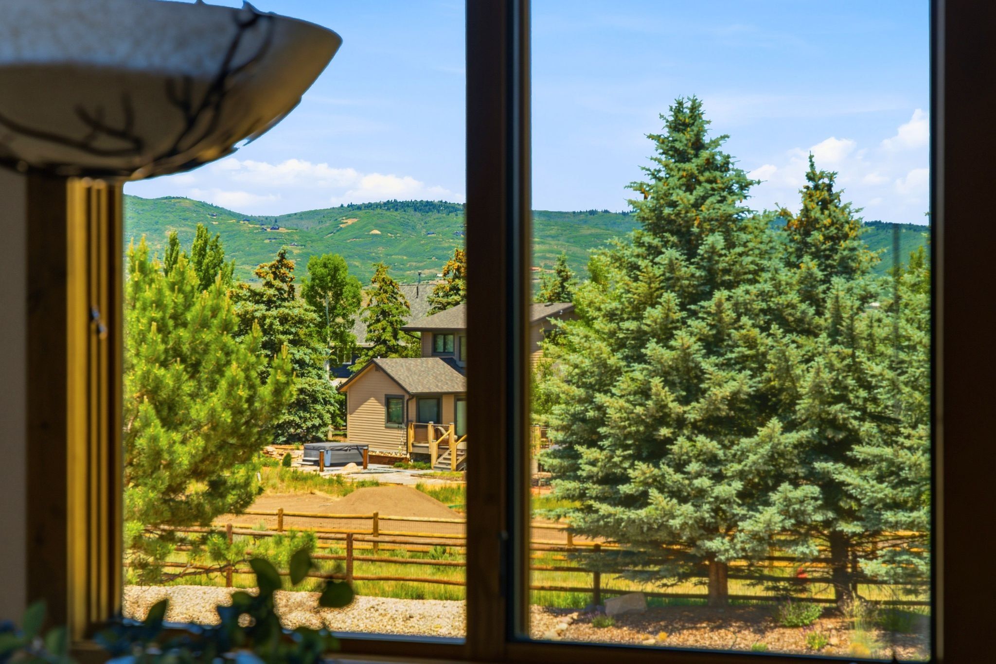 Expansive window framing a mountain backdrop with mature evergreen trees and a rustic wooden fence