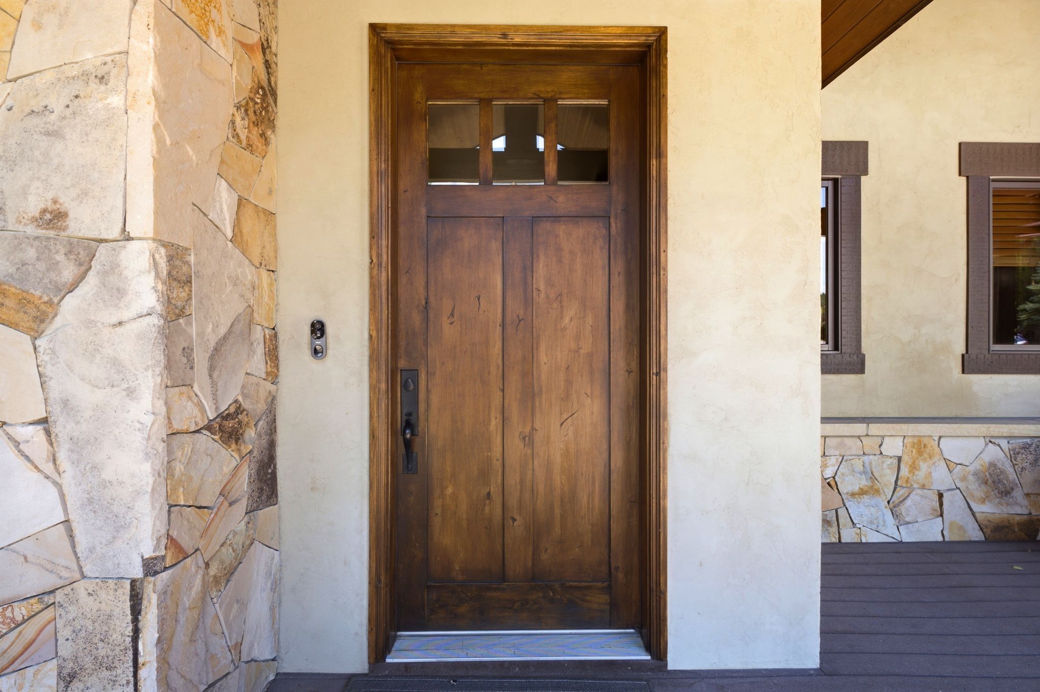 Craftsman-style wood entry door with clear glass transom panels, set within a stucco facade