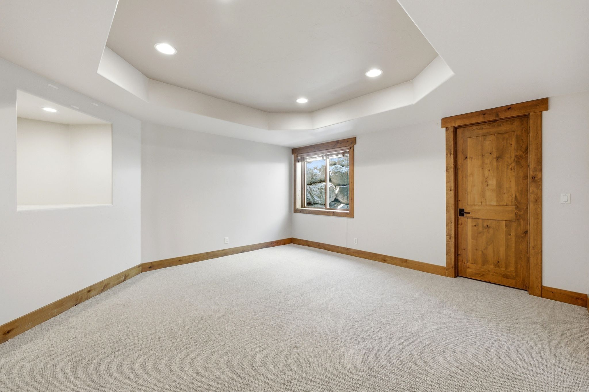 Spacious room featuring light-toned carpeting, white walls, and a tray ceiling with recessed lighting