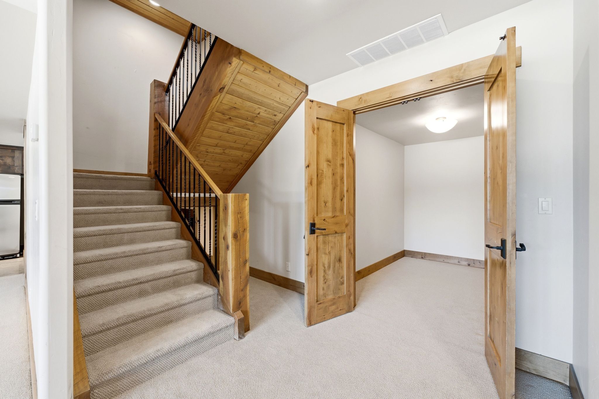 Staircase featuring carpeted treads, wood-finish risers, and black metal balusters
