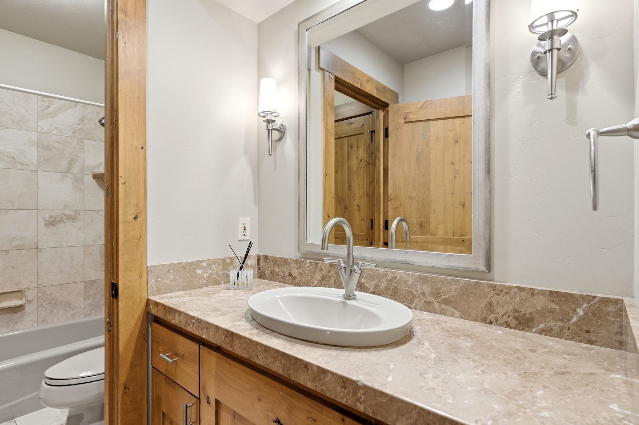 Bathroom vanity featuring a light-toned stone countertop with an oval under-mount sink and brushed nickel faucet