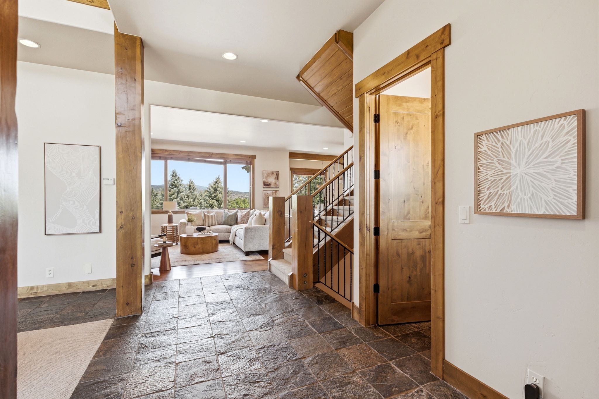 Entryway featuring slate flooring, exposed wood columns, a wood-framed doorway, and a visible staircase with wood newel posts and metal balusters