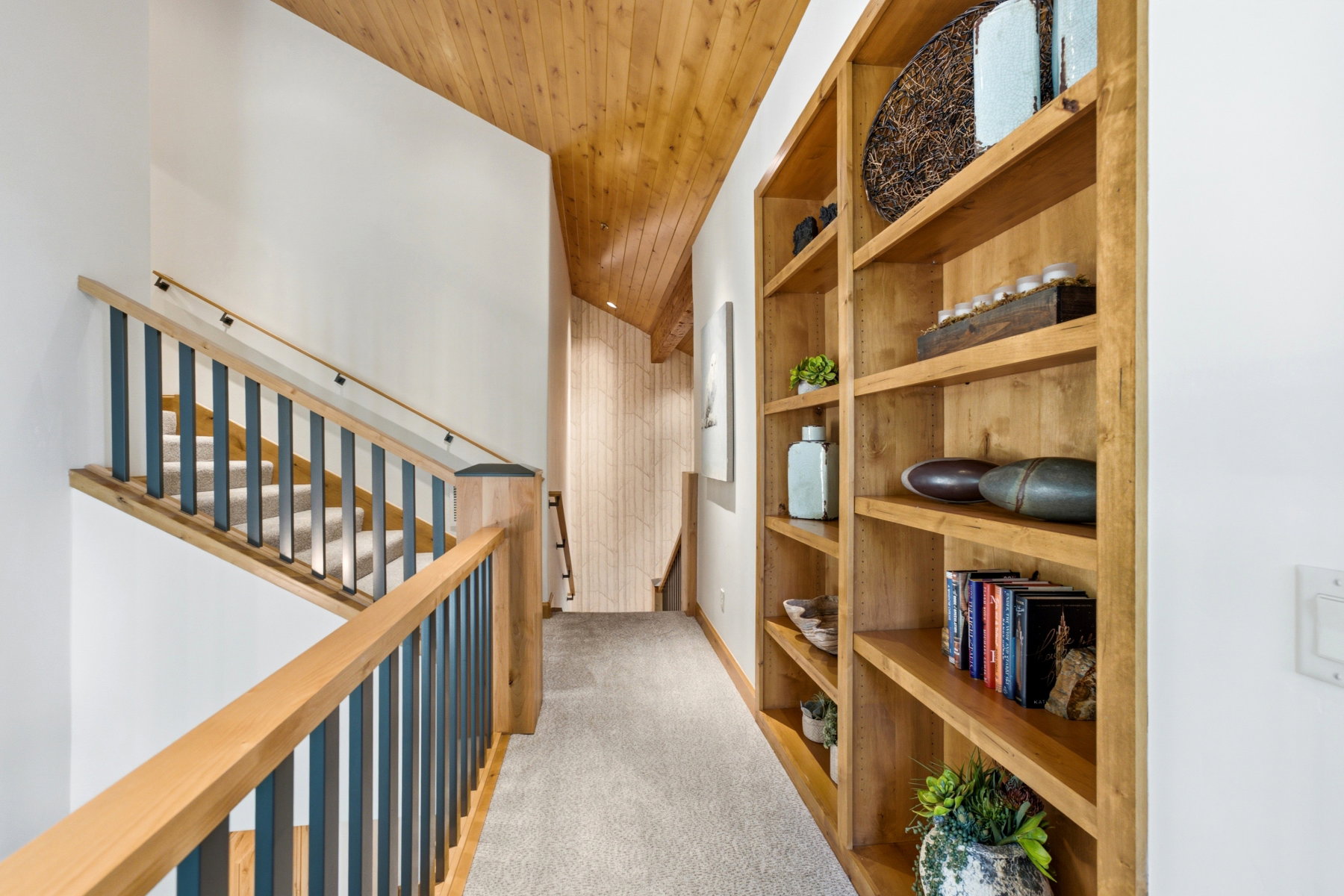 Upper-level hallway featuring a vaulted wood-paneled ceiling, light-toned carpet flooring, and custom built-in shelving
