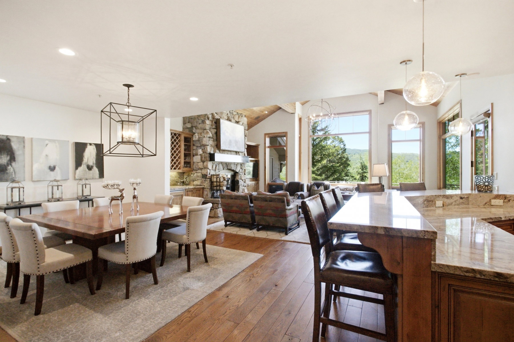 Expansive open-concept living area featuring wood-finish flooring, a stone fireplace, and large windows showcasing exterior scenery