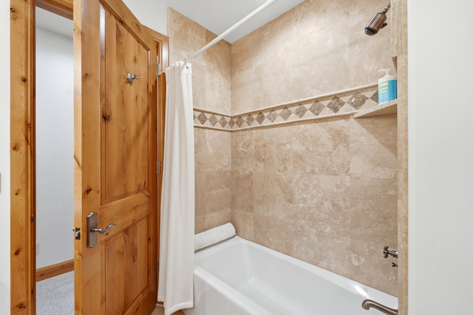 Bathtub and shower combination featuring neutral-toned tile surround, decorative accent tile band, and a built-in shower niche