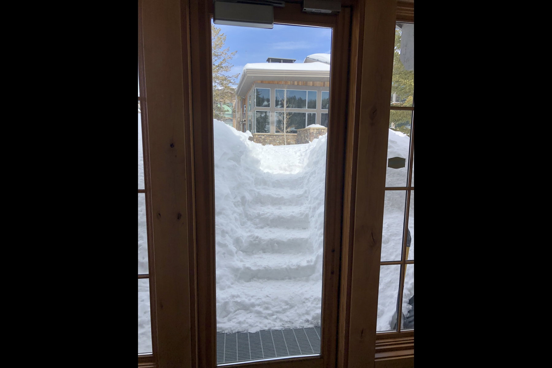 Wood-framed glass-paneled door with a view of snow-covered steps and a building exterior featuring multiple windows