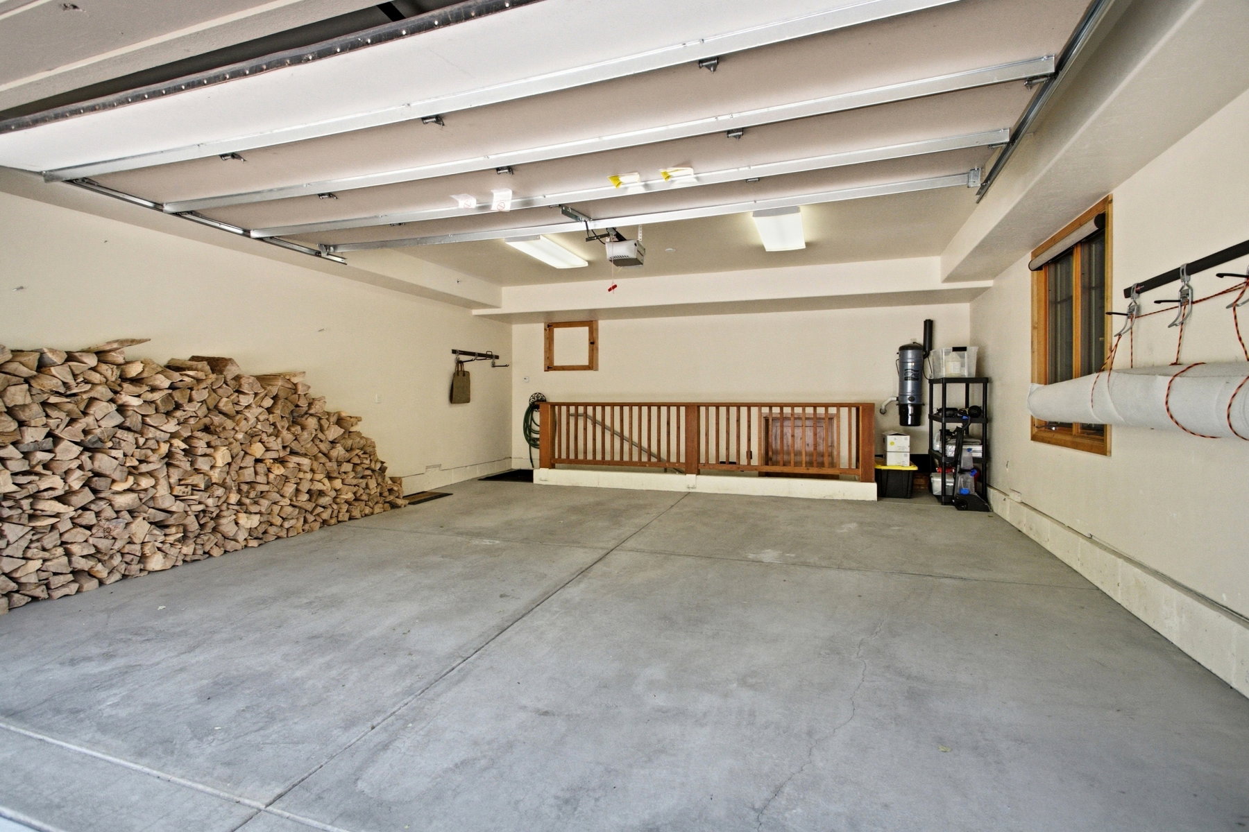 Spacious garage with concrete flooring, overhead lighting, a built-in wooden railing, and a framed window