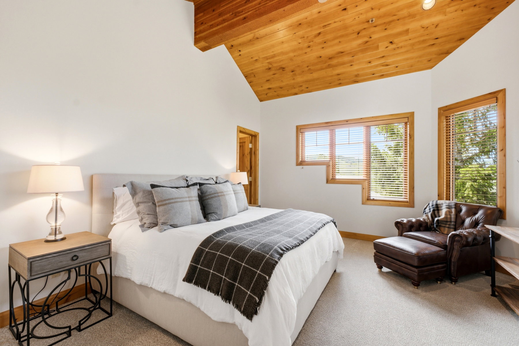 Vaulted wood-paneled ceiling with exposed beam, multiple windows with wood trim, and neutral-toned wall paint