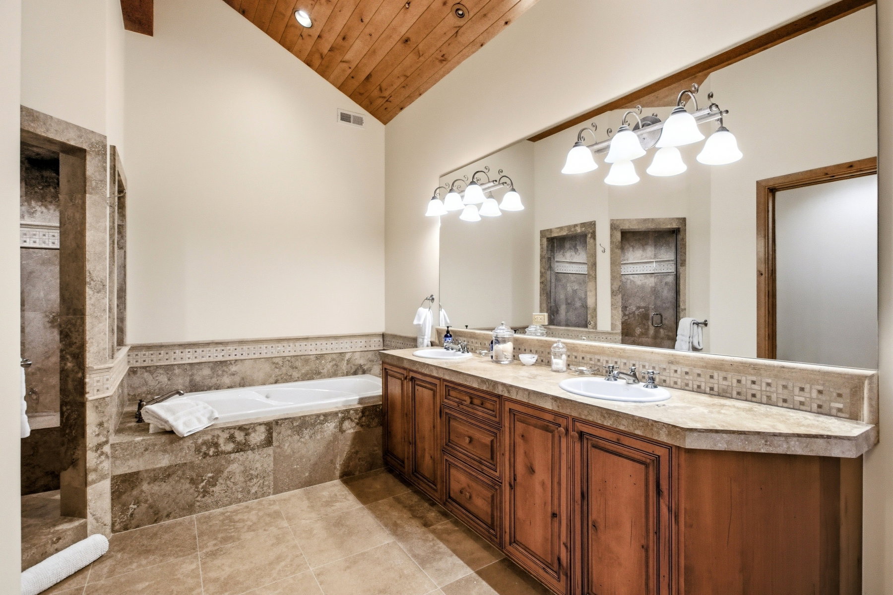 Spacious bathroom featuring a vaulted wood-plank ceiling with exposed beam, dual vanities with integrated sinks, a built-in tub, and a separate walk-in shower